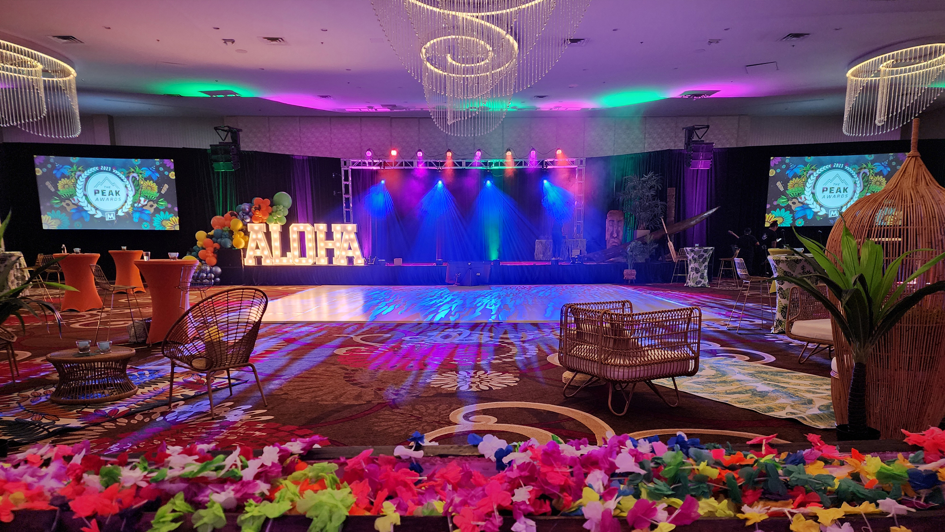 A tropical-themed indoor celebration. Large lit-up letters spell ALOHA